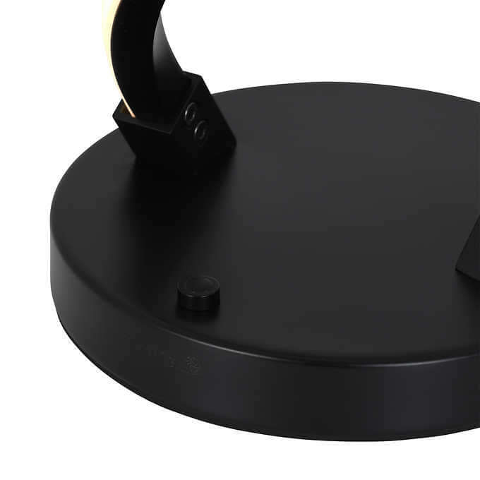 A close-up of a black lamp base with a button and part of the lamp's curved, glowing armature visible.