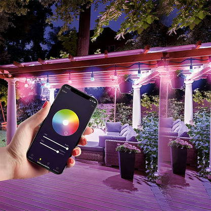 An outdoor evening setting with a smartphone in the foreground displaying a color wheel app, controlling the pink hue of smart lights draped over a pergola.