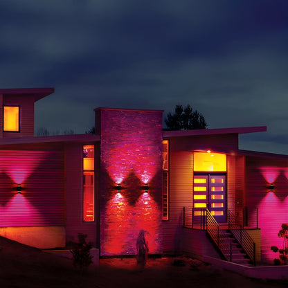 The image depicts a modern house at dusk illuminated with vibrant pink and orange lights, casting dynamic shadows on the exterior walls.